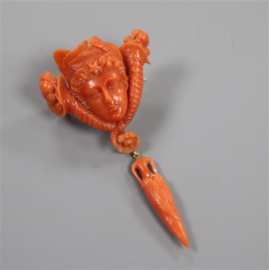 A 19th century carved coral drop brooch, modelled as the head of a lady between two cornucopia with foliate drop, 75mm.